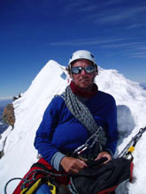 Steve Hunt on the summit of Mt Cook with Middle Peak and prayer flags behind him